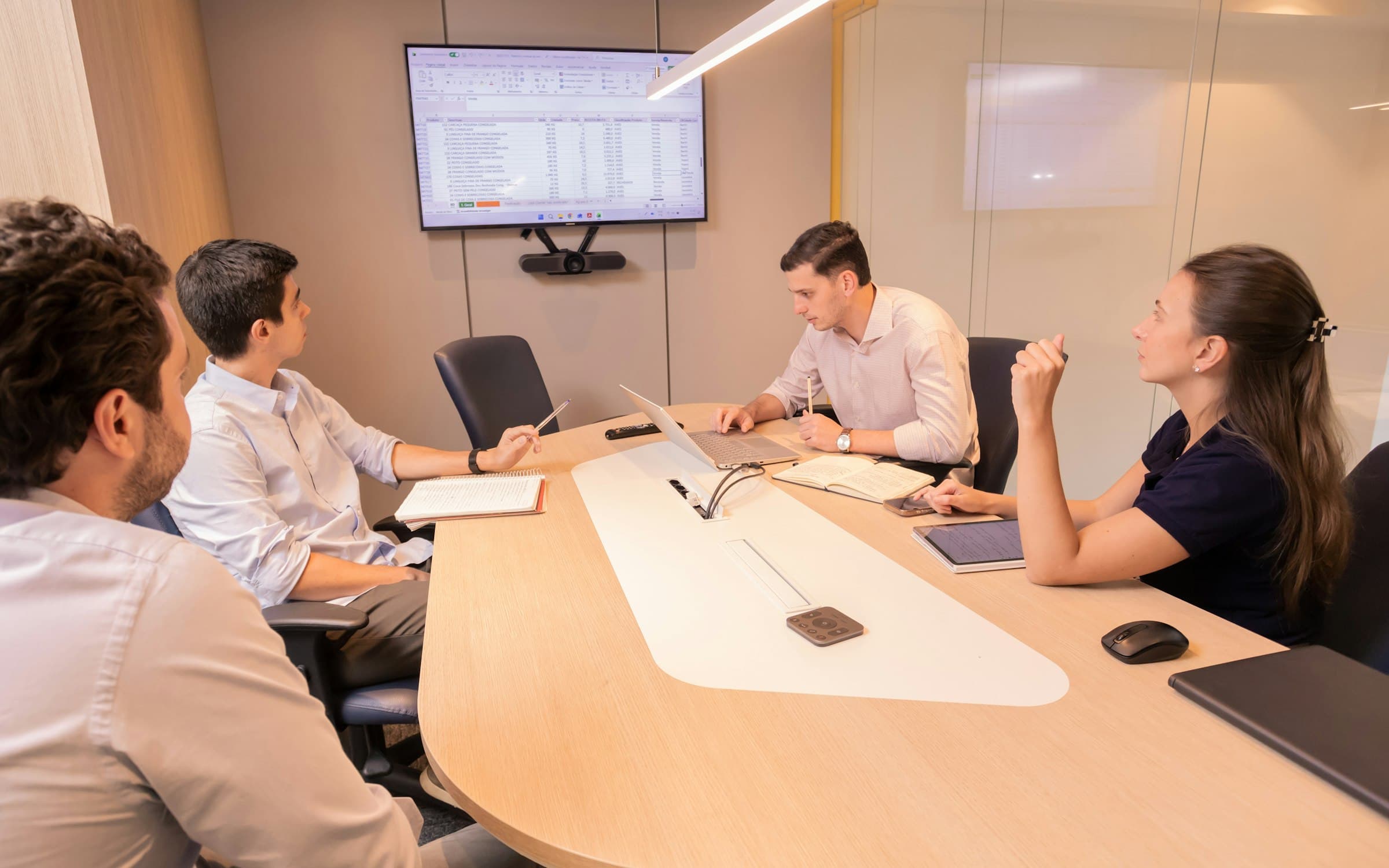 Équipe en réunion de coordination autour d'un écran de planning et d'ordinateurs portables dans une salle de réunion