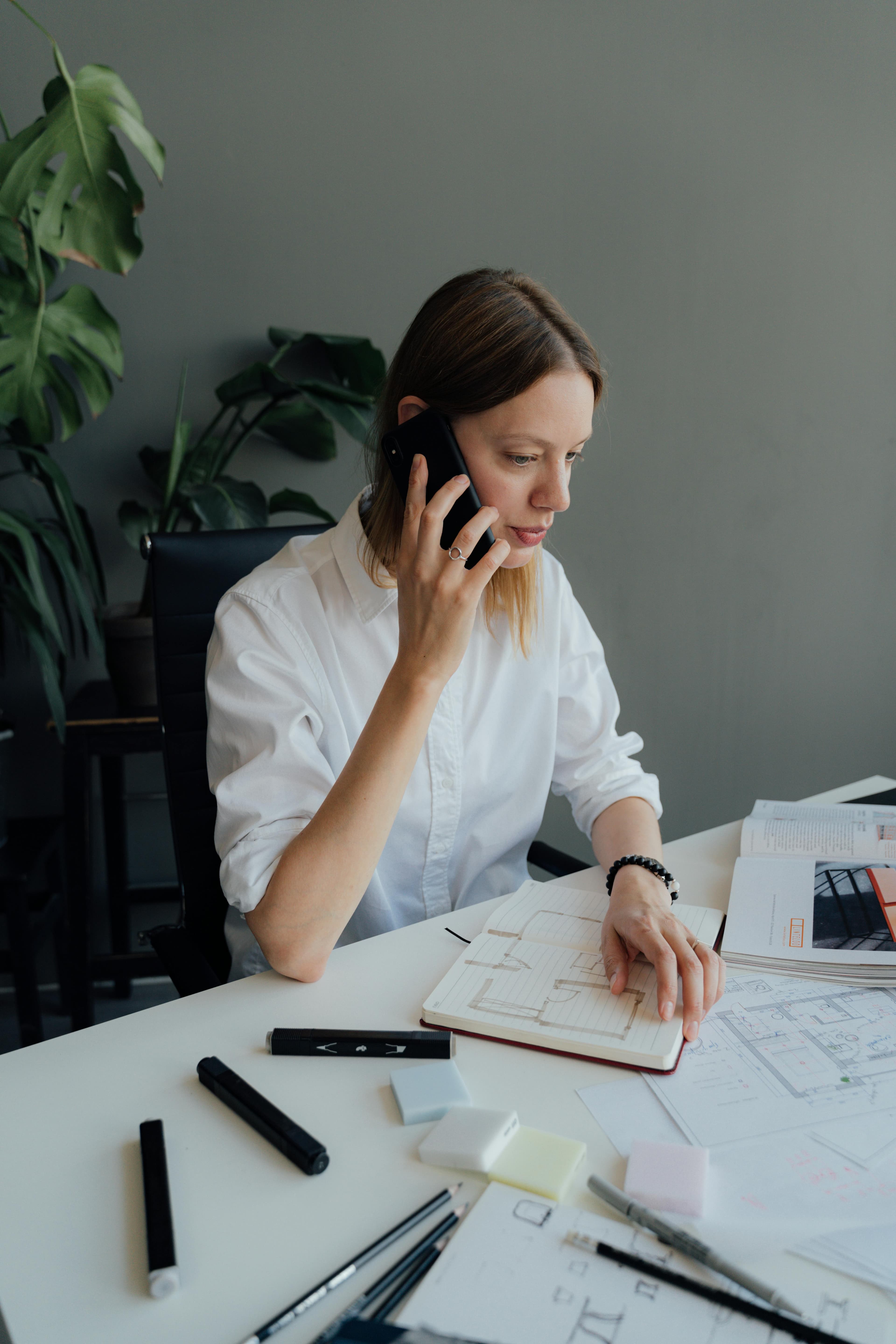 Bureau de travail avec documents étalés, carnet ouvert et combiné posé pour un échange téléphonique discret