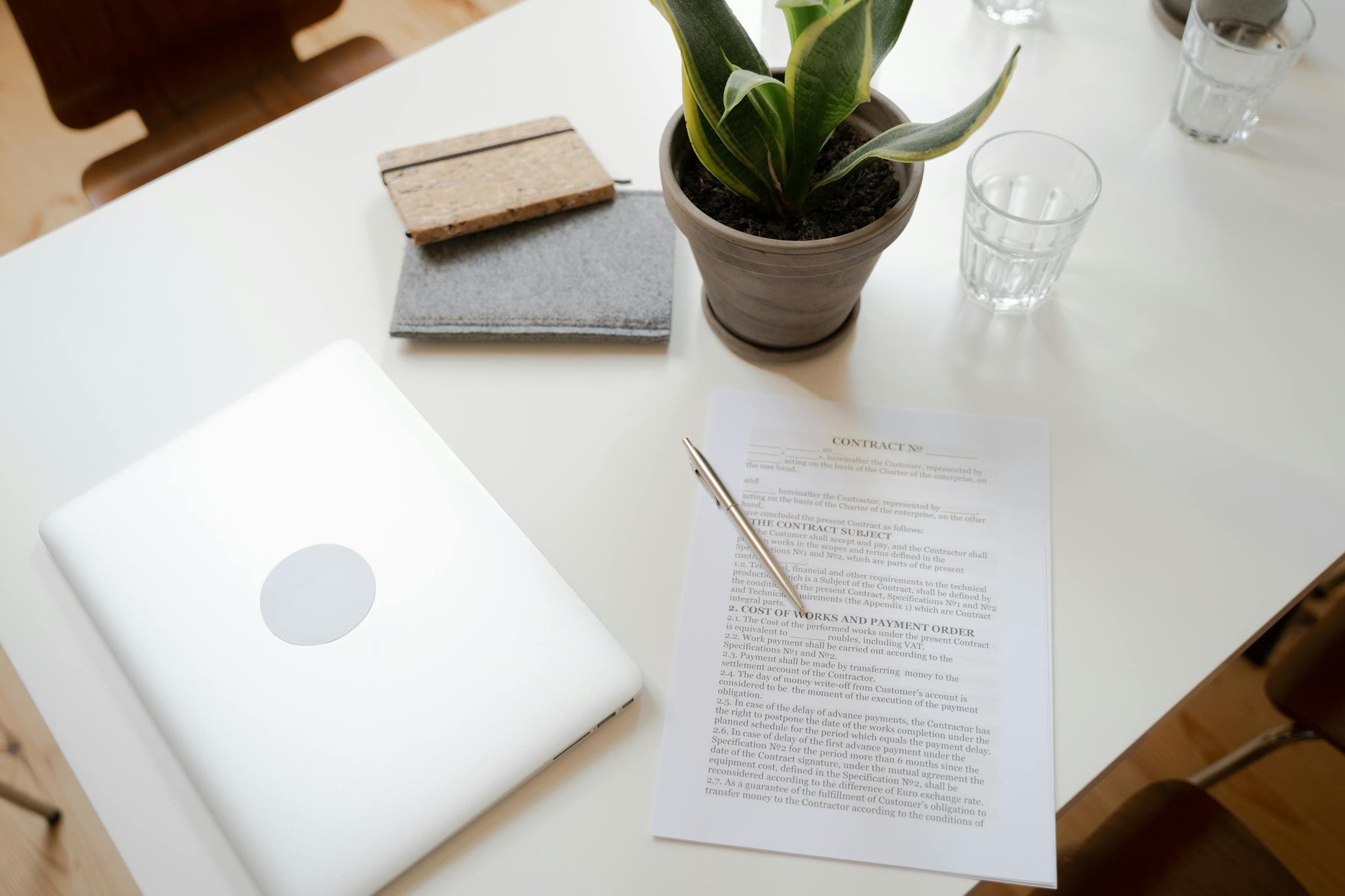 Bureau épuré avec laptop, contrat signé et plante posés sur une table blanche